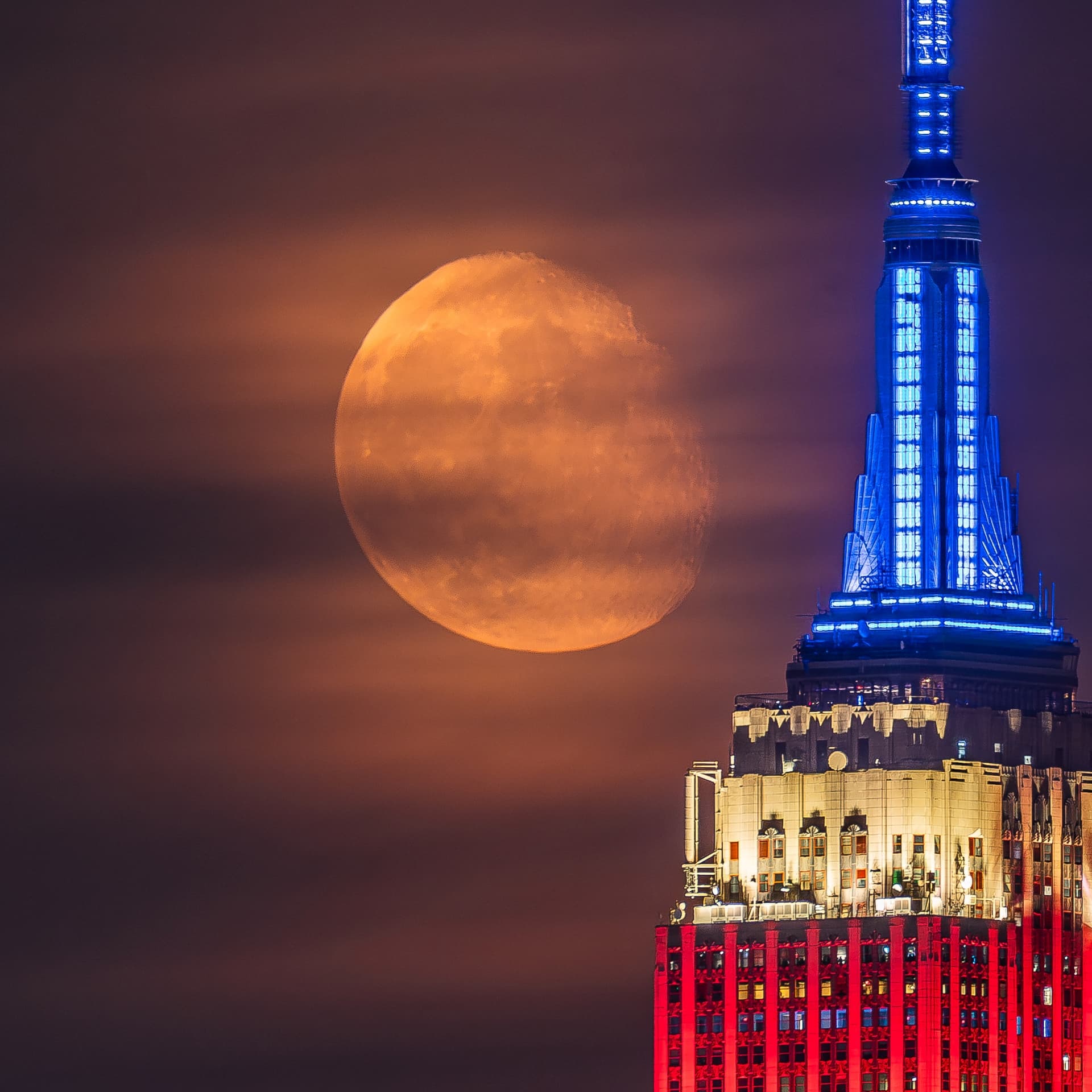 The moon next to the Empire State Building lit in red, white, and blue.