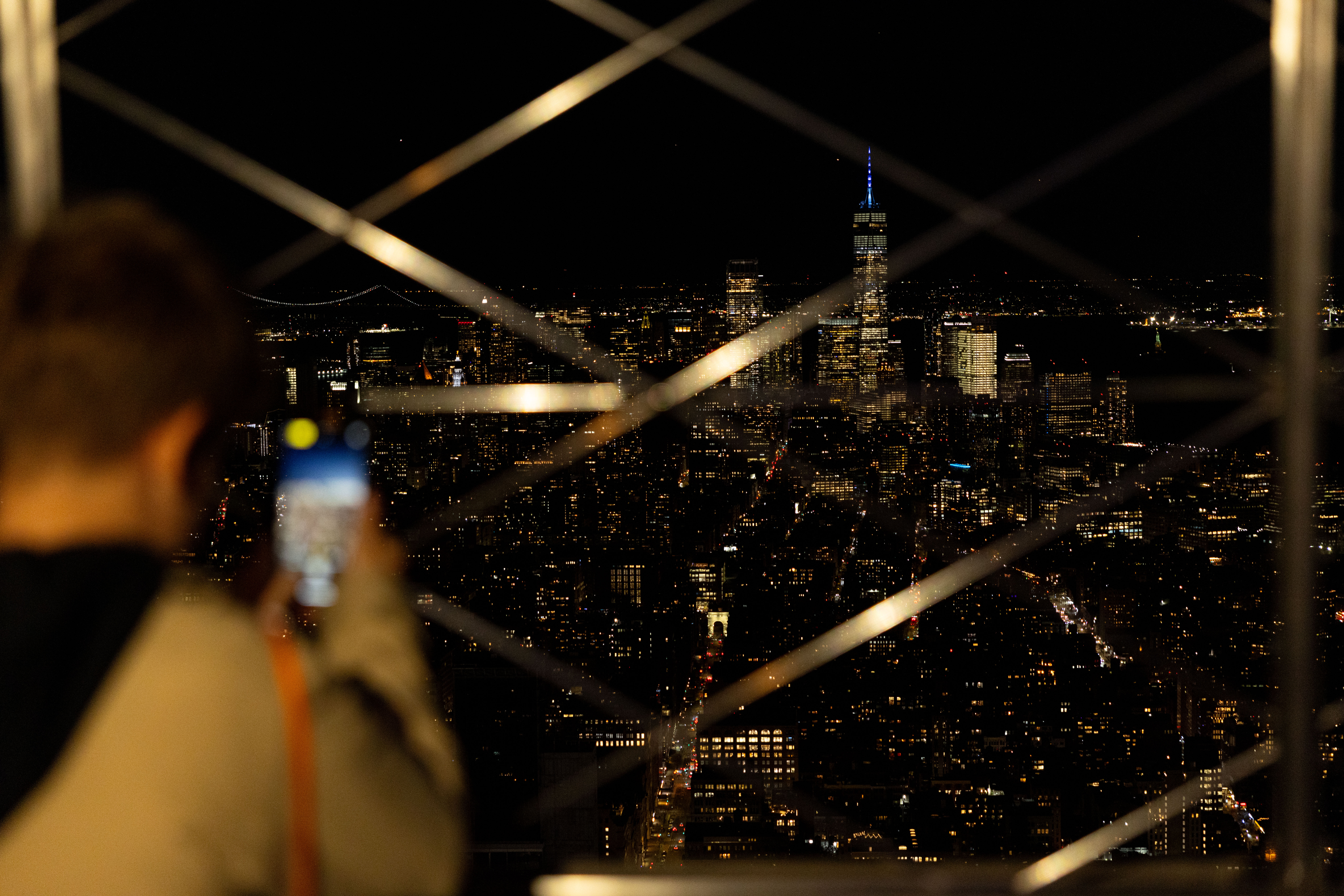 Person taking photo of the NYC night time skyline from the Empire State Building Observation Deck