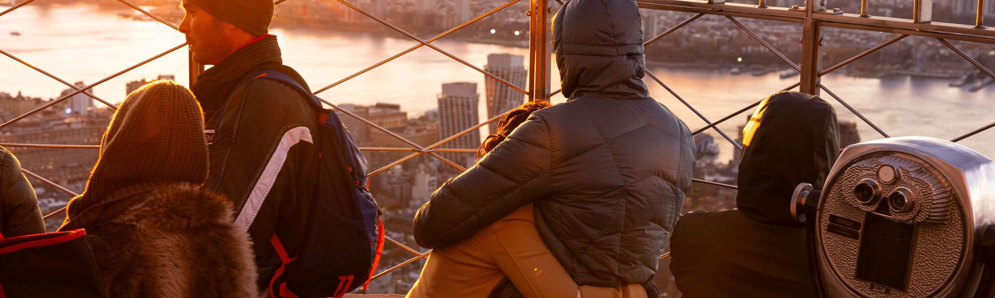 People looking out at NYC from the 86th floor observation deck at the Empire State Building Observatory.