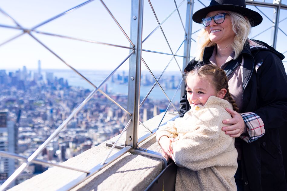 People looking out at NYC from the 86th floor observation deck at the Empire State Building Observatory.