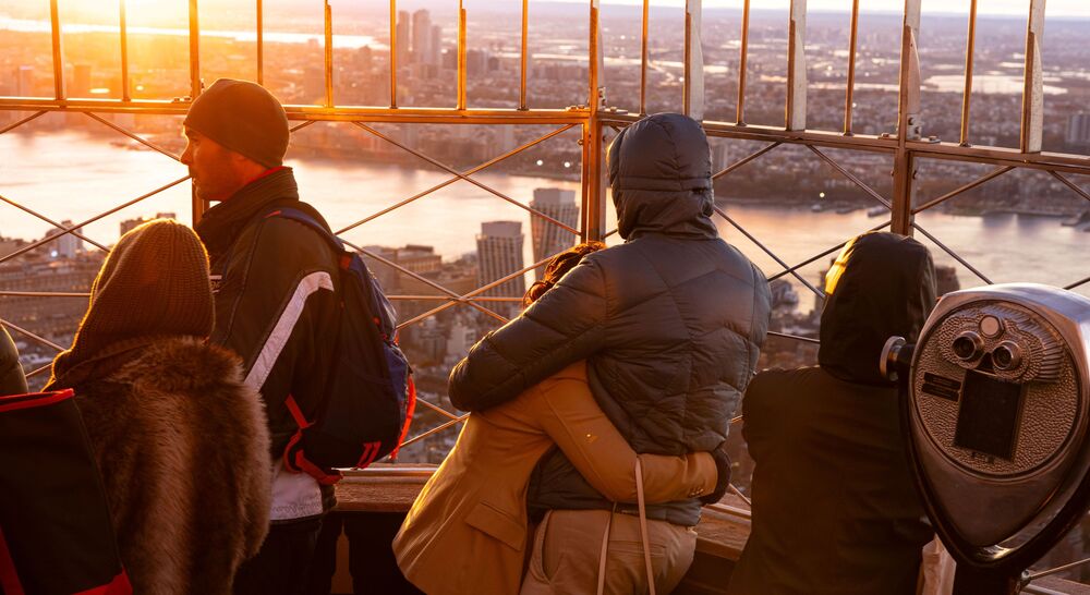 People looking out at NYC from the 86th floor observation deck at the Empire State Building Observatory.