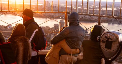 People looking out at NYC from the 86th floor observation deck at the Empire State Building Observatory.
