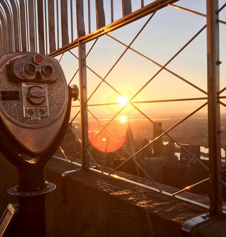 Binoculars next to a view of the sunrise at the Empire State Building