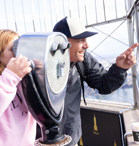 People looking out at NYC from the 86th floor observation deck at the Empire State Building Observatory.