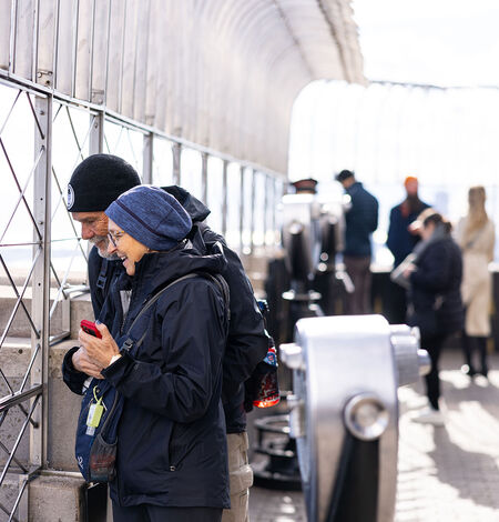People looking out at NYC from the 86th floor observation deck at the Empire State Building Observatory.
