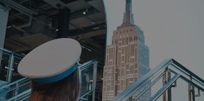 woman wearing a white hat looking up at the Empire State Building from an outdoor staircase