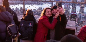 People looking out at NYC from the 86th floor observation deck at the Empire State Building Observatory.