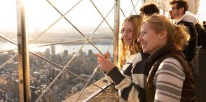 People looking out at NYC from the 86th floor observation deck at the Empire State Building Observatory.
