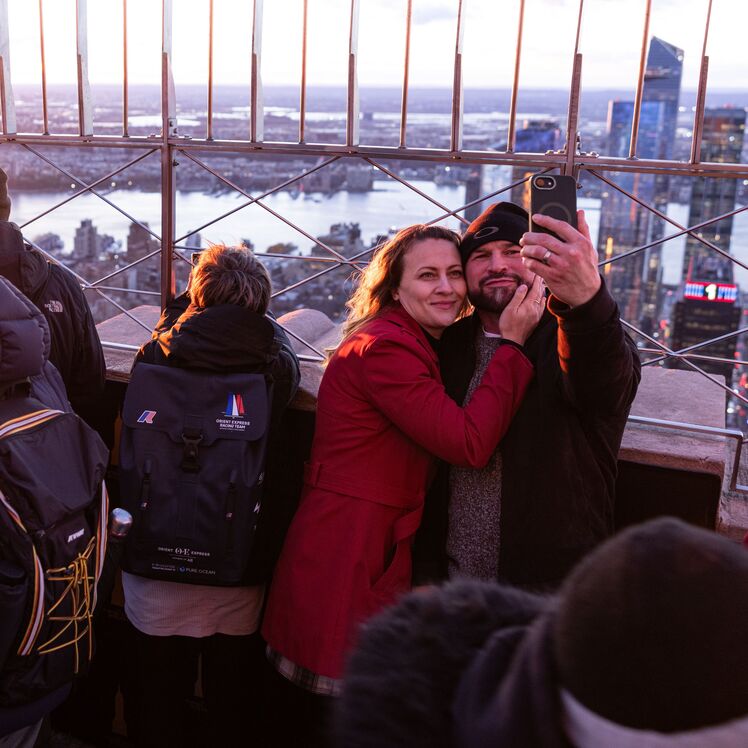 People looking out at NYC from the 86th floor observation deck at the Empire State Building Observatory.